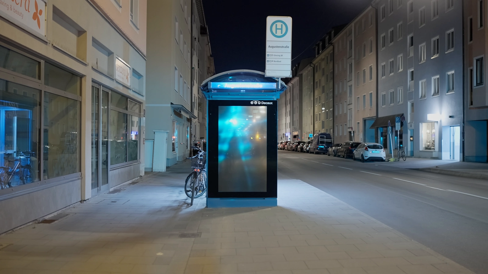 A deactivated advertising display stands at the centre of an empty Munich street at night.