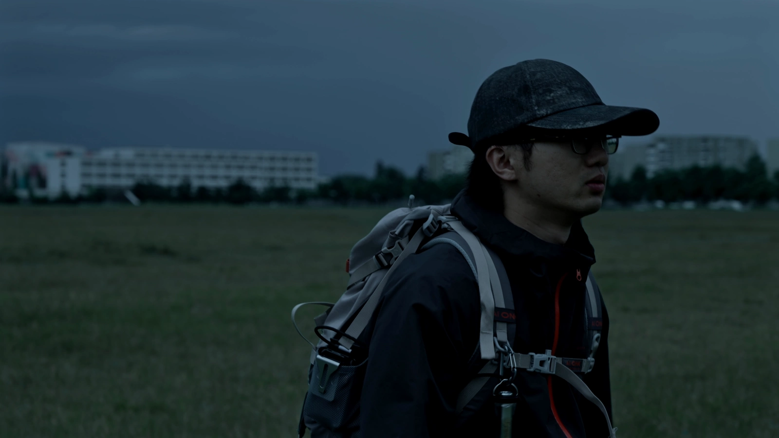 A figure carrying a portable projector crosses an open field beneath a dark blue sky.