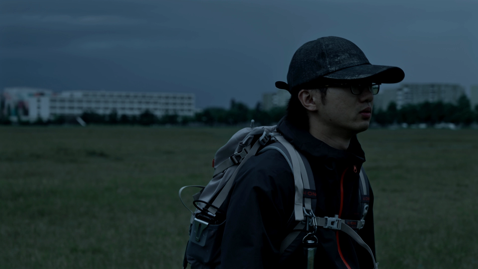 A figure carrying a portable projector crosses an open field beneath a dark blue sky.