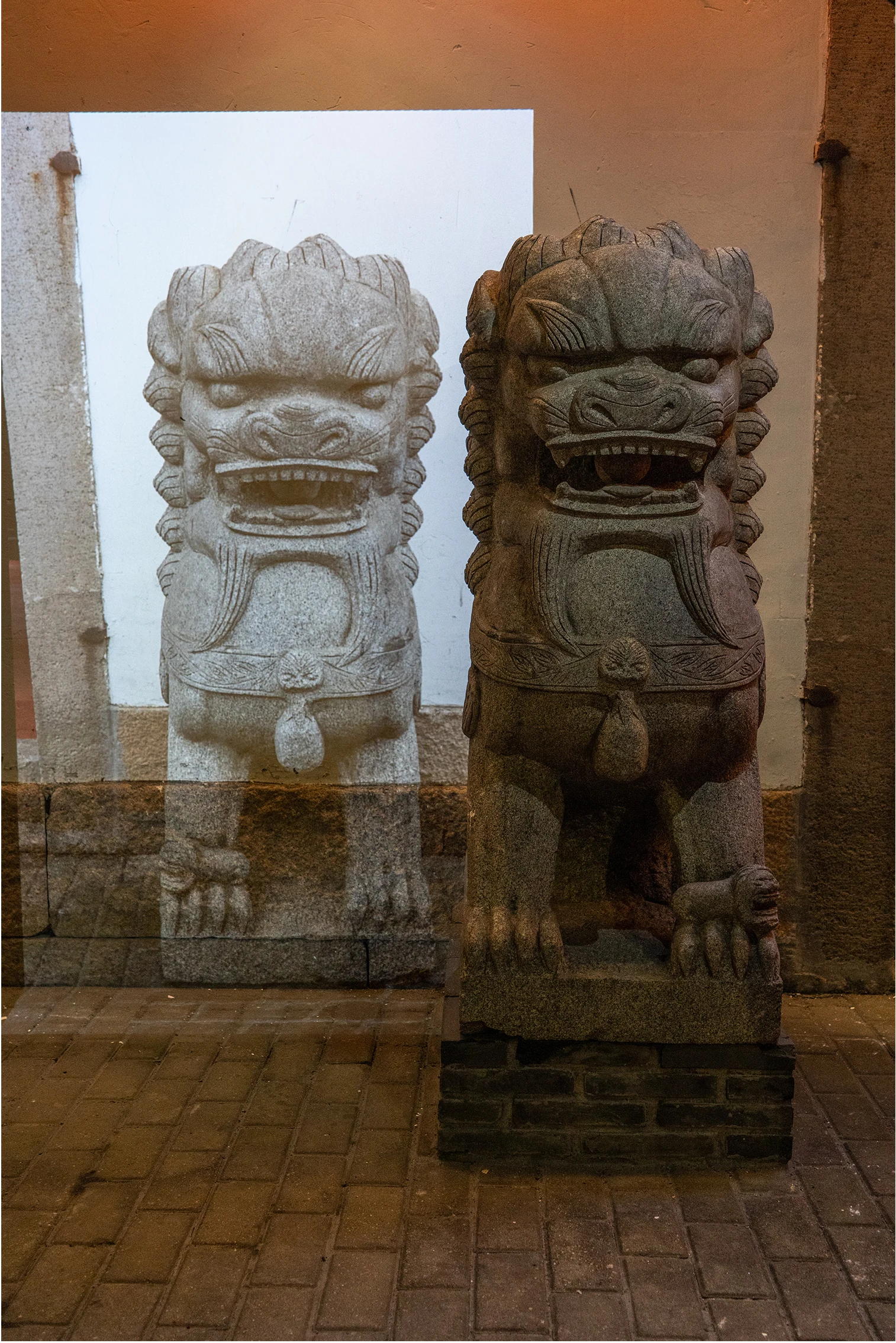Two female lion figures, one sculptural and one projected, overlap at a building entrance.