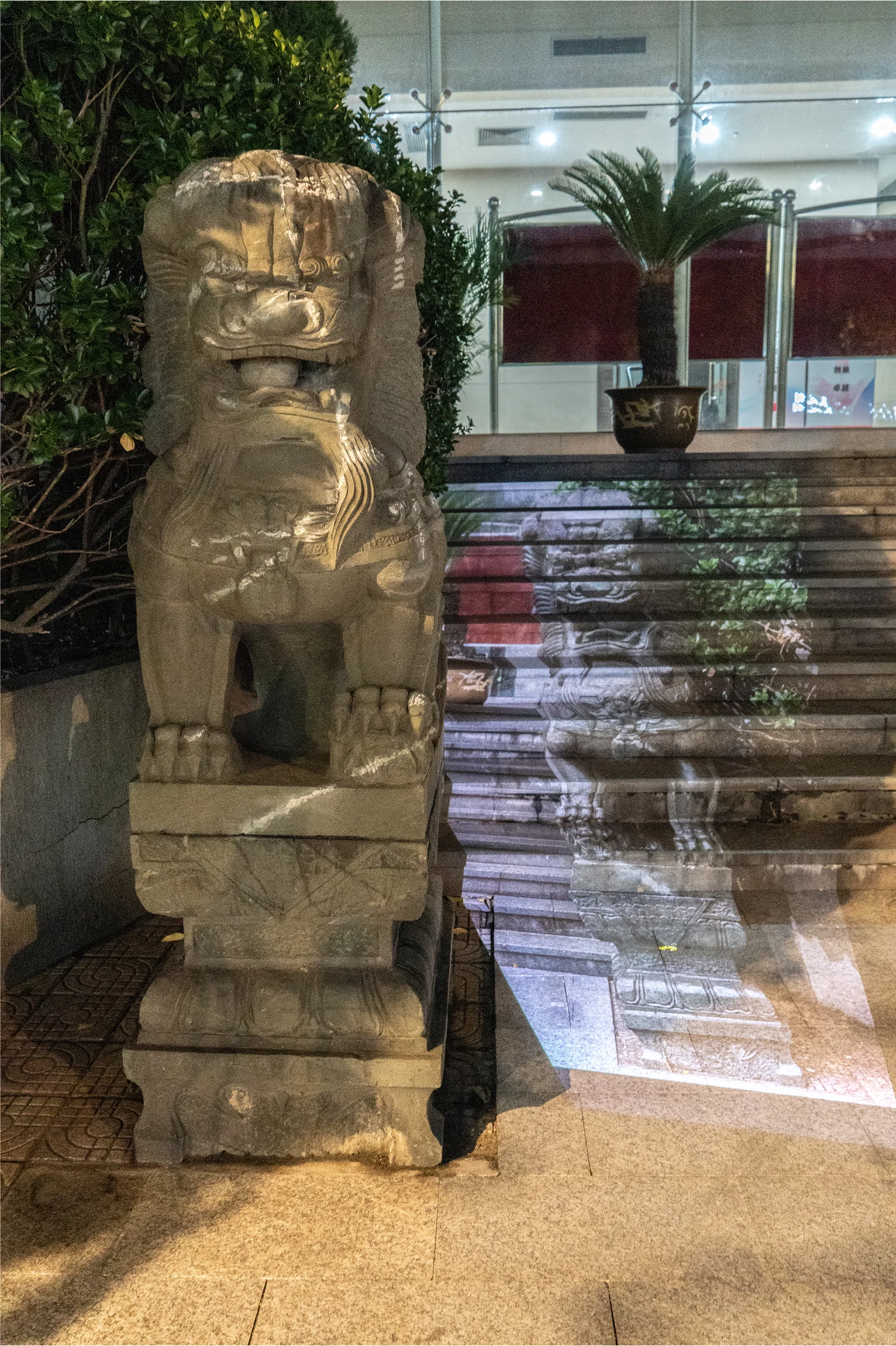 A stone lion and a projected lion appear together beside an entrance and steps.