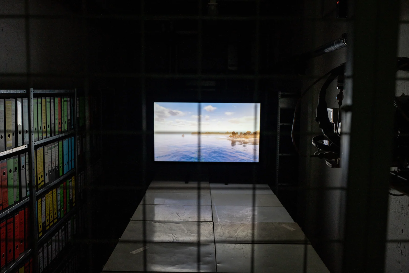 A television showing a blue digital landscape sits within a dark installation.