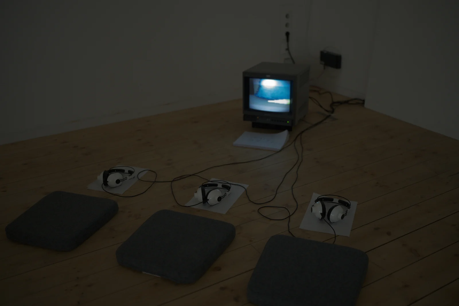 A CRT television, headphones and printed paper are arranged in the corner of a room.