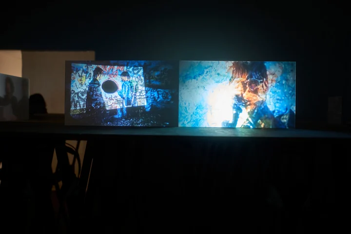 A figure and projected textures appear across a pair of illuminated panels.