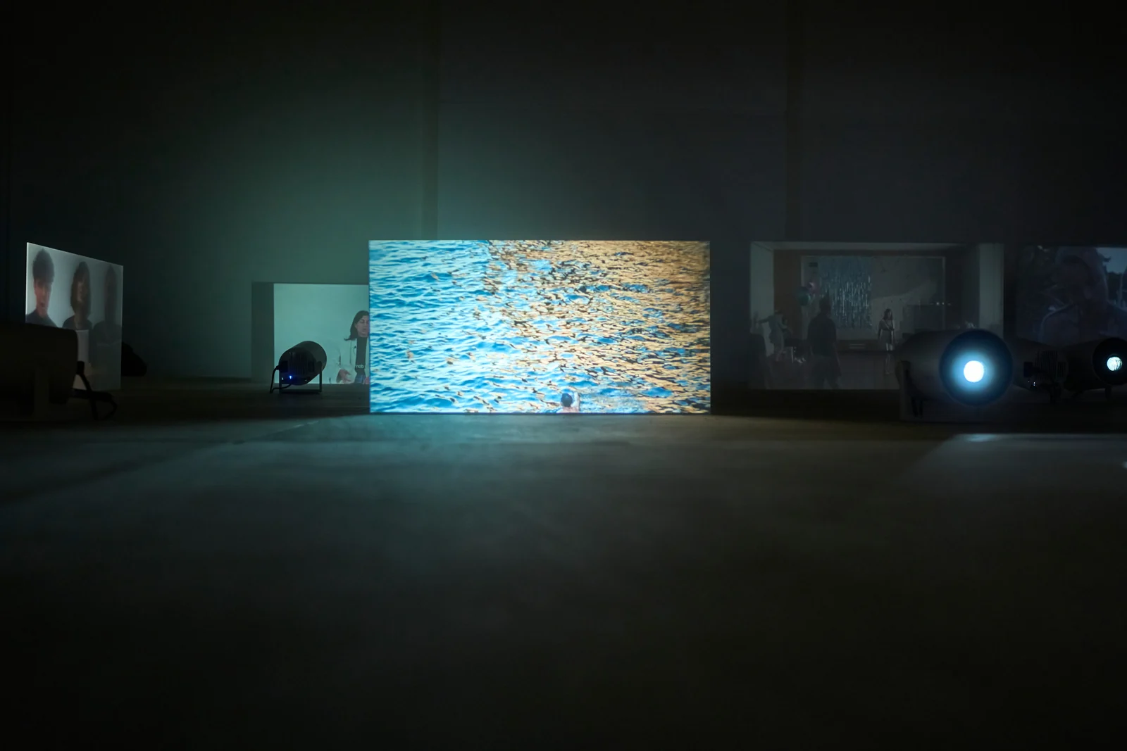A rectangular projection of sunlit water in a dark exhibition space.