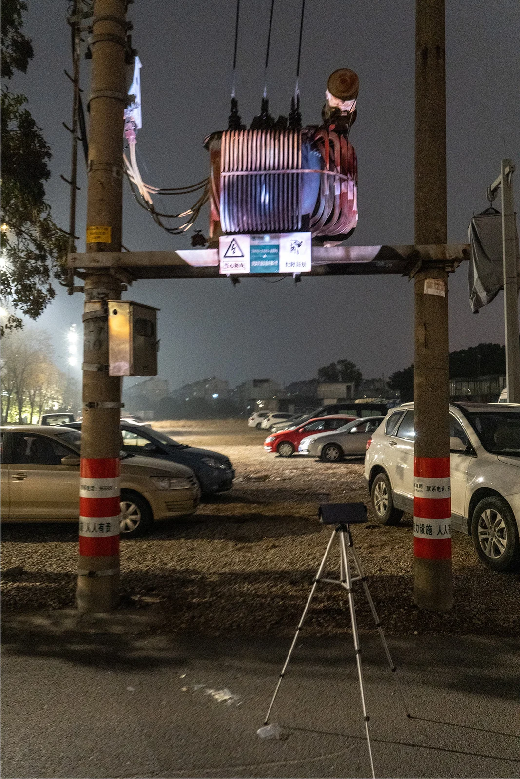 A tripod projects onto an electrical transformer suspended between two poles at night.