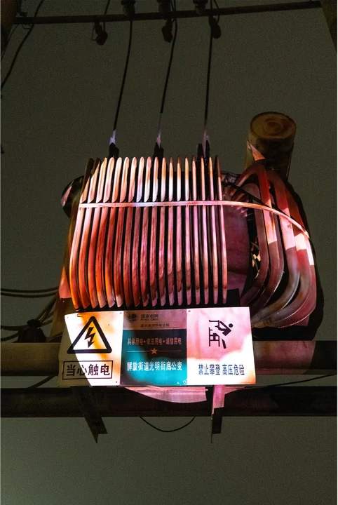 A projection follows the ribbed metal surface of an electrical transformer.