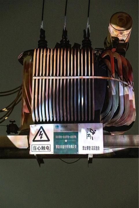 Projected light falls across the metal fins and cables of a transformer.