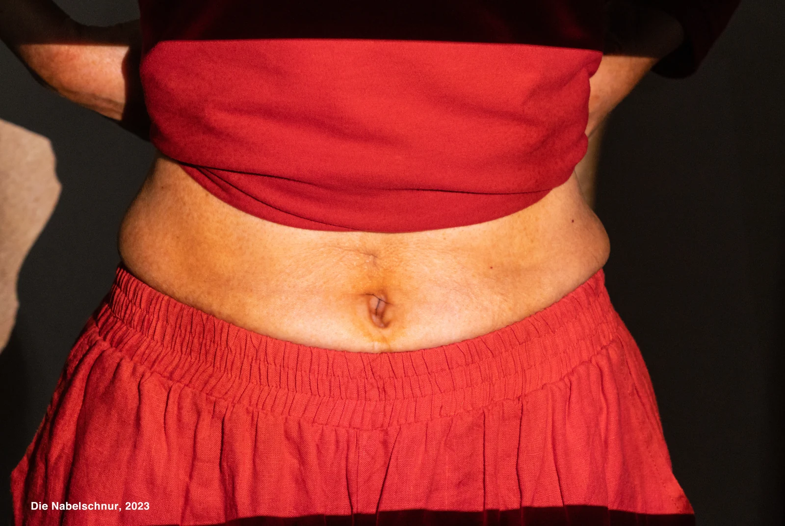 A projected image of an umbilical cord falls across a belly, framed by red clothing.