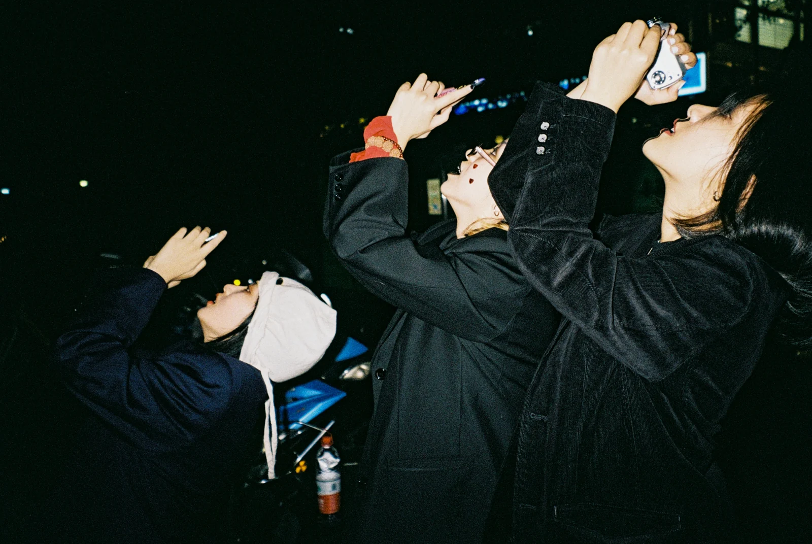 Three young people raise their hands and cameras into the night.