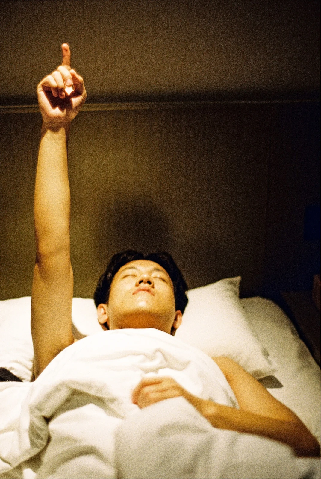 A person in bed points one arm upwards.