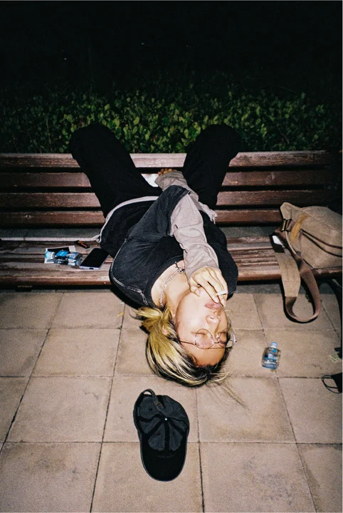 A person lies upside down across a park bench.
