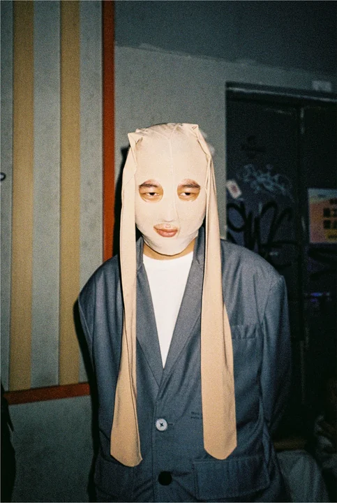 A person wears a cloth mask in a flash-lit portrait.