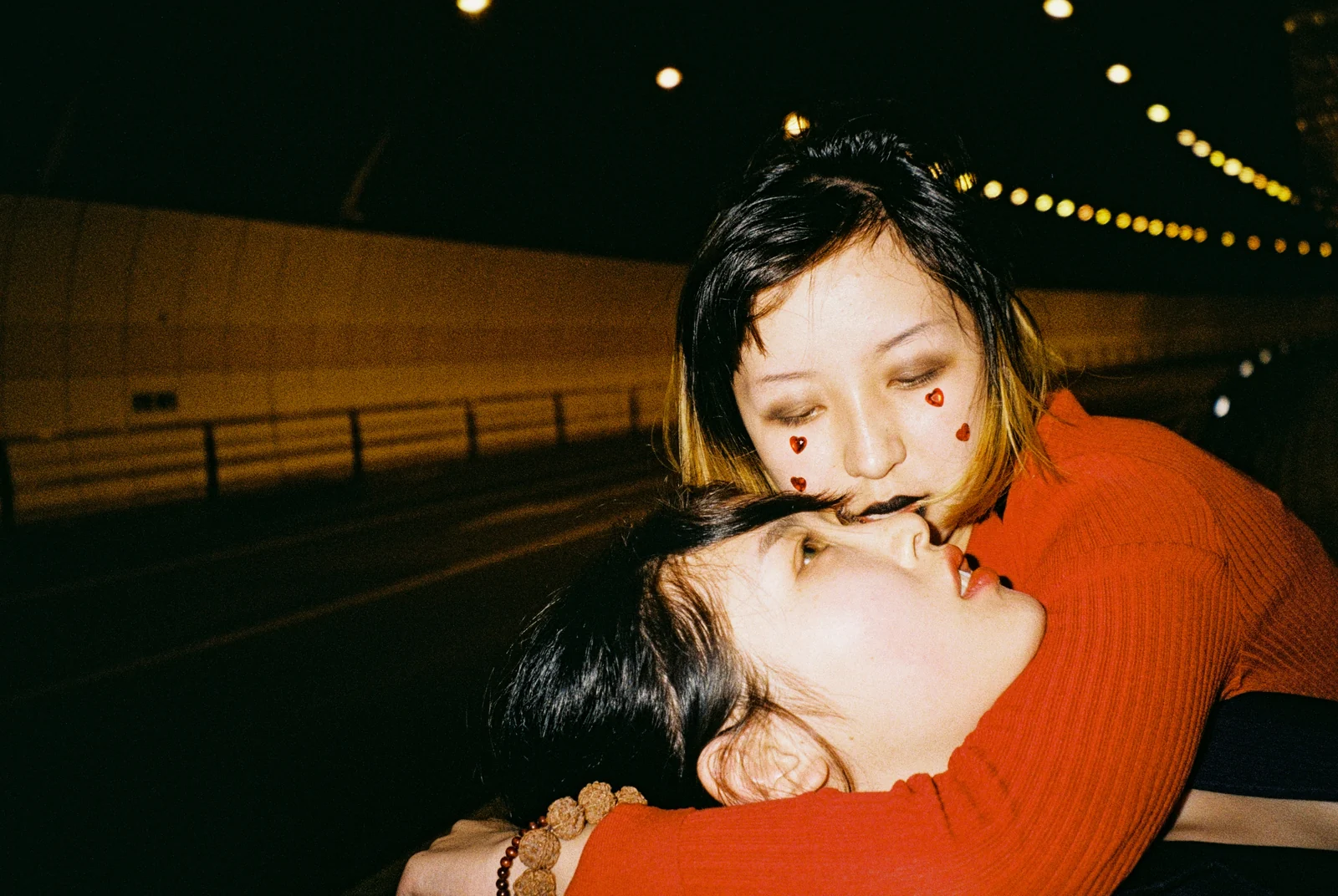 Two young people embrace under the lights of a nighttime walkway.