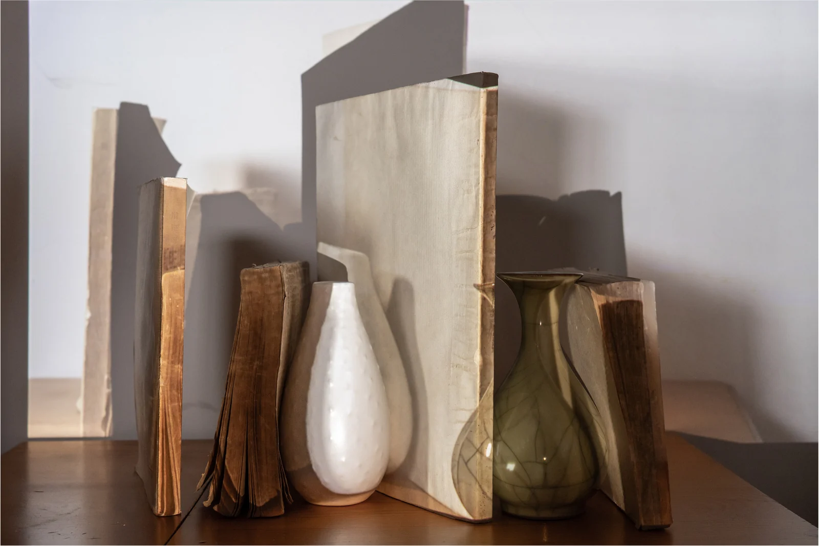 Vases and books overlap with projected images and shadows on a tabletop.