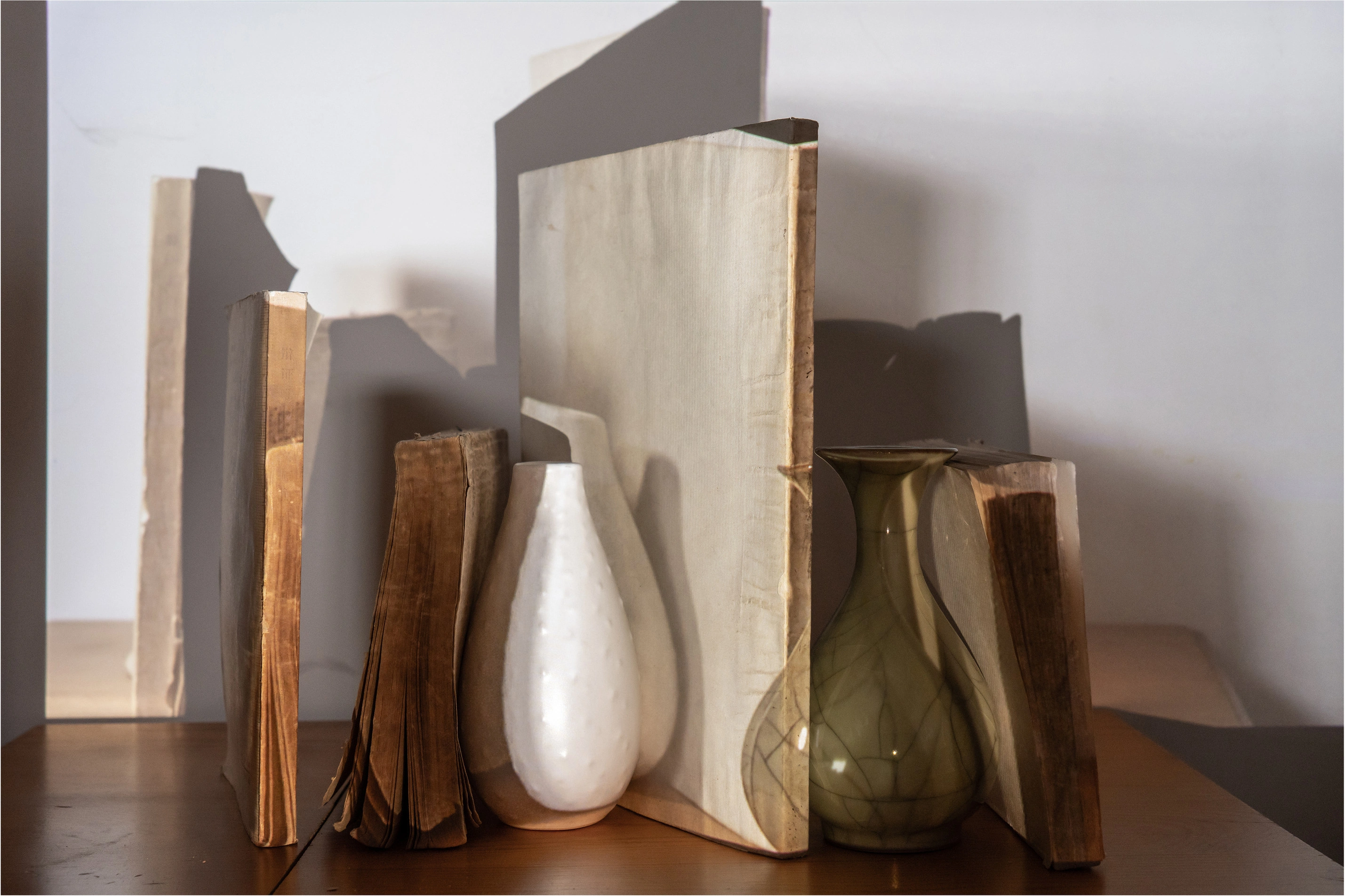 Vases and books overlap with projected images and shadows on a tabletop.