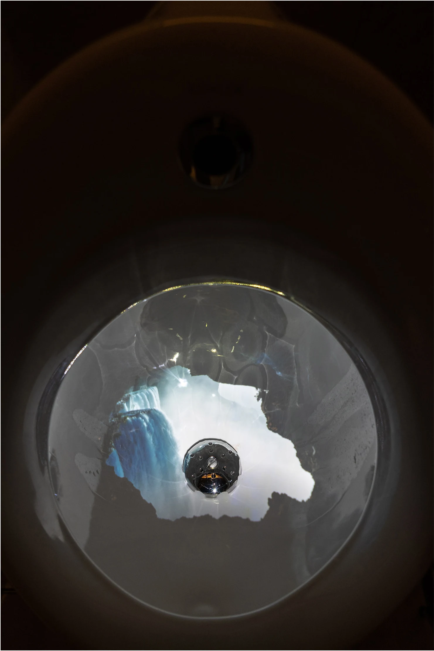 An image of flowing water is projected into a white ceramic basin.