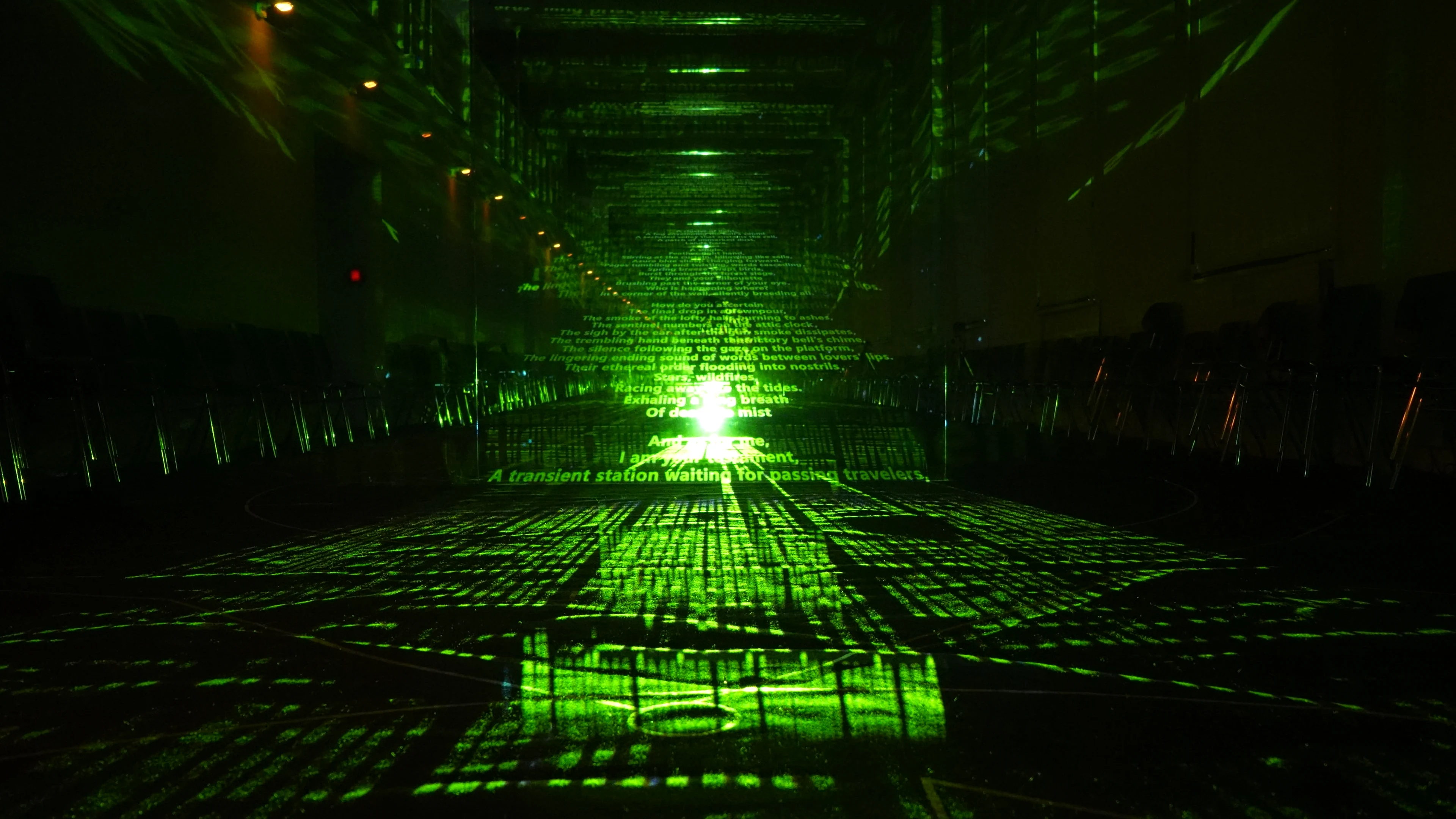 Green text and light extend symmetrically across the floor and walls of a dark exhibition space.